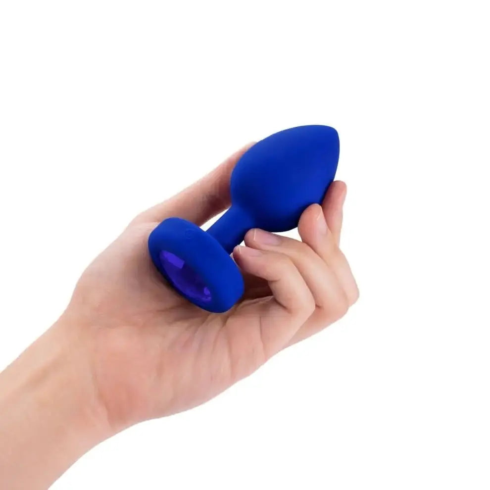 A hand holding a blue plastic finger displayed with the b-Vibe Vibrating Jewel Plug