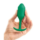 A hand holding a green plastic bottle next to b-Vibe Weighted Snug Plug 2 - 114 Grams