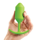 Hand holding a green plastic bottle beside b-Vibe Weighted Snug Plug 3 (180 grams)