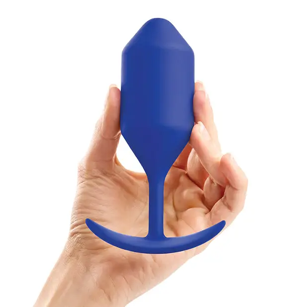 A hand holding a blue plastic bottle paired with b-Vibe Weighted Snug Plug 4’s smooth grip handle