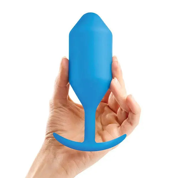 Hand holding b-Vibe Weighted Snug Plug 5 - 350 Grams, blue plastic rocket shape