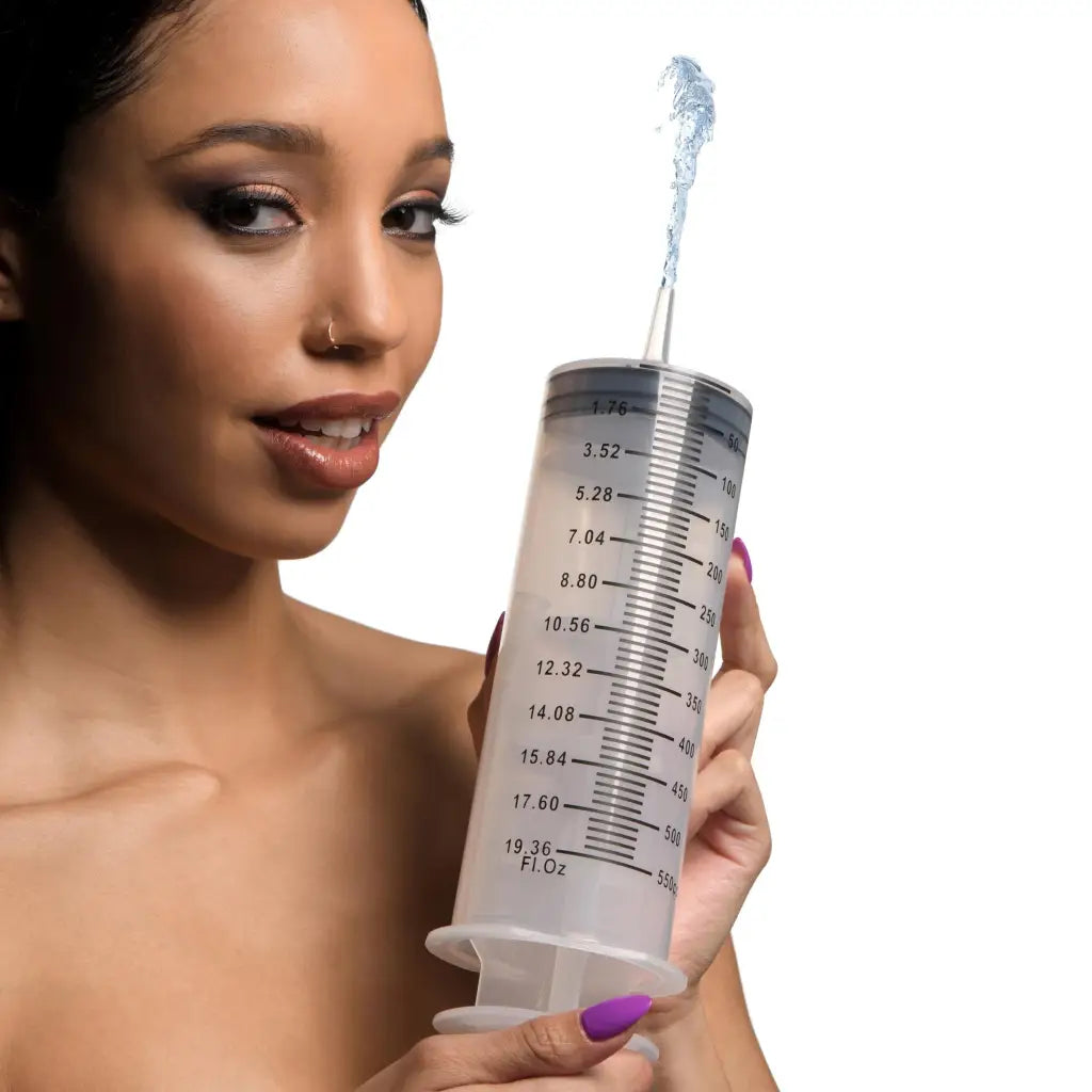 Woman holding oversized enema syringe with measurement markings and silicone tube