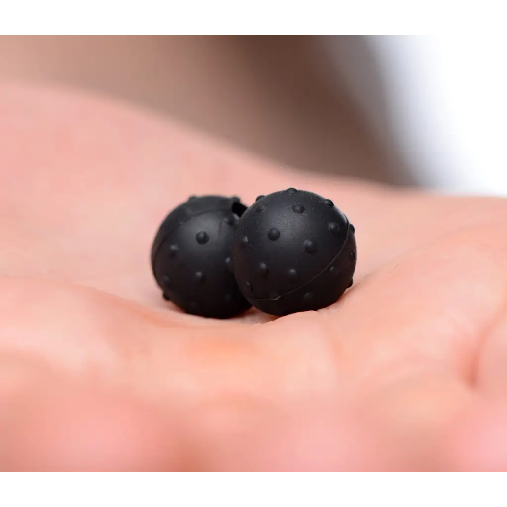 Orbs Nubbed Silicone Magnetic Balls: Two small black spheres with textured surfaces on a palm