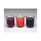 Three lit scented candles from the Master Series Flame Drippers Candle Set in purple, red, and black