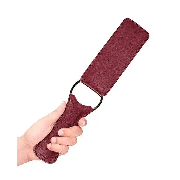 Burgundy Ouch Halo Paddle with loop handle from Shots Ouch, held in a hand