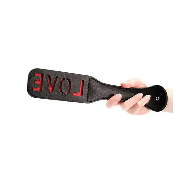 Hand holding Shots Ouch Love Paddle - Black with ’LOVE’ embossed in red