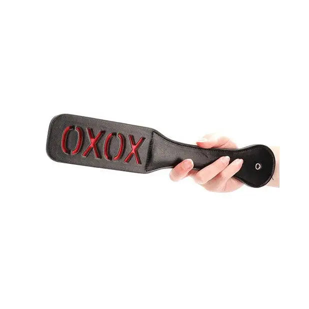 Hand holding Shots Ouch Xoxo Paddle - Black, featuring ’OXOX’ text in leather