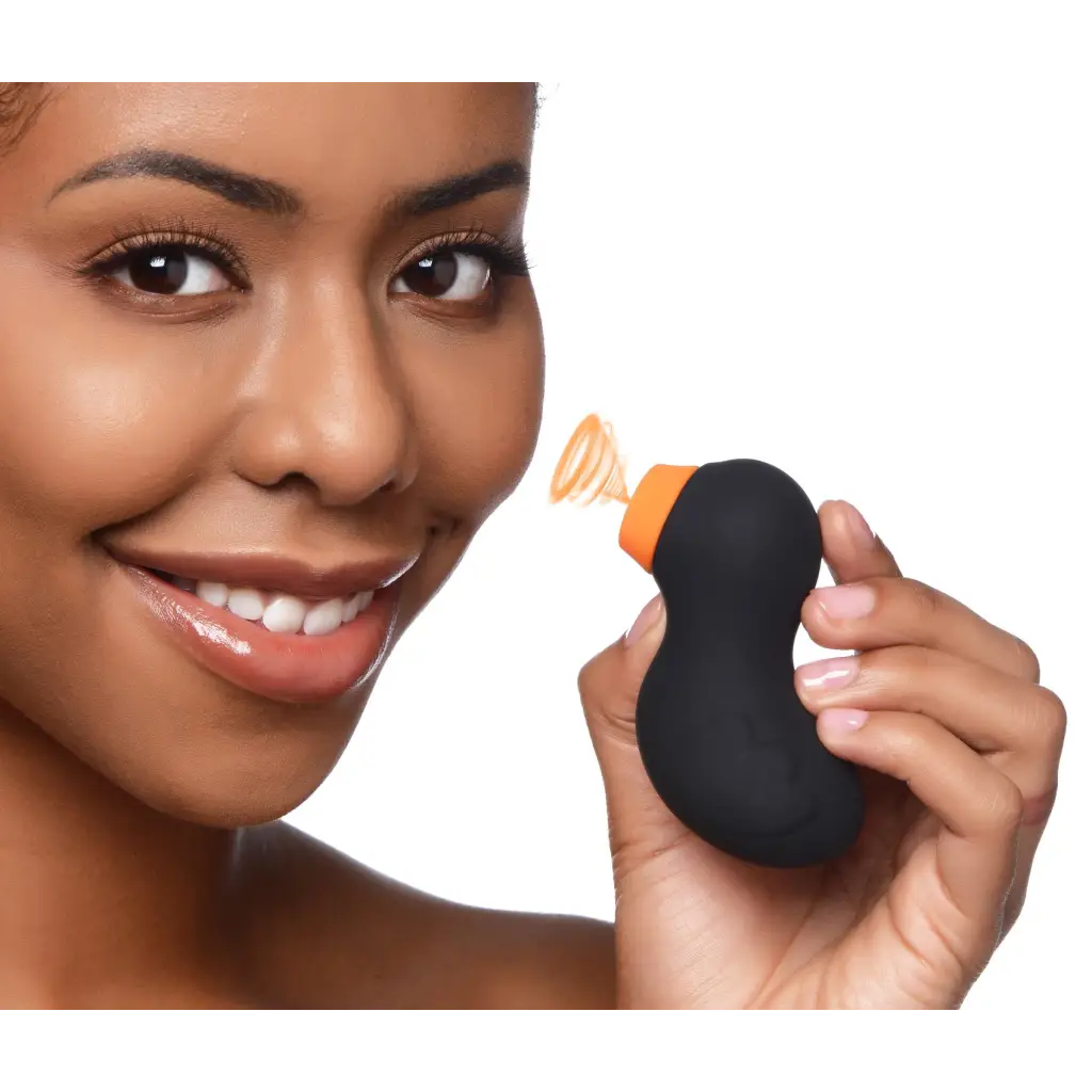 Black, kidney-shaped Sucky Ducky Clitoral Stimulator sponge with orange stem held by hand