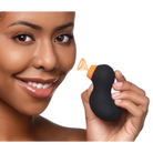 Black, kidney-shaped Sucky Ducky Clitoral Stimulator sponge with orange stem held by hand