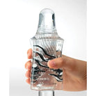 Hand holding Tenga Crysta Block - Clear glass bottle with a decorative swirling pattern