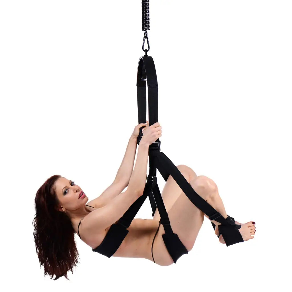 A woman in a black bikini uses the Trinity Vibes Sex Swing while suspended by a rope